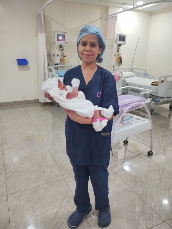 Dr. Payal Aggarwal in hospital scrubs holding a newborn